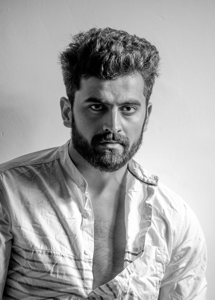Black and white portrait of a South Asian man with facial hair and stylish attire, evoking a strong and confident look.